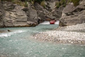 A jetboat at full speed between cliffs on the Shotover River in Queenstown, New Zealand