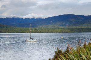 One little boat on lake Te Anau with forest and snow-capped mountains in the background